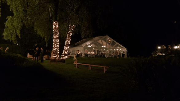 Tent wedding lighting. Tree wraps in Christmas lights with a tent lit by chandeliers.