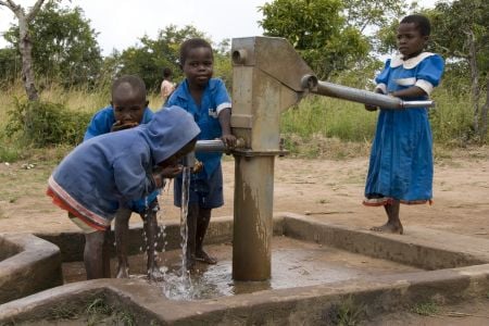Happy children drinking water from a borehole pump in Zimbabwe, drilled by Plan Canada International clean water initiative programs.
