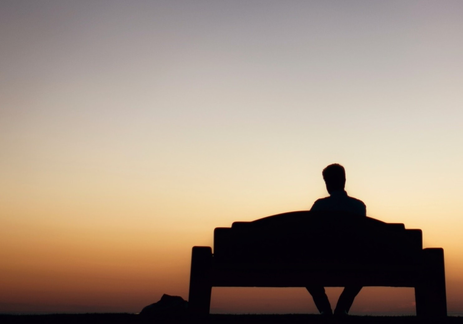 Person seated on a bench outside at sunset