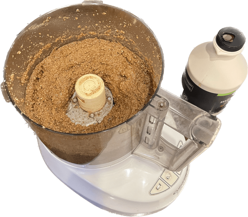 Food processor with pecan butter and maple syrup container next to it.