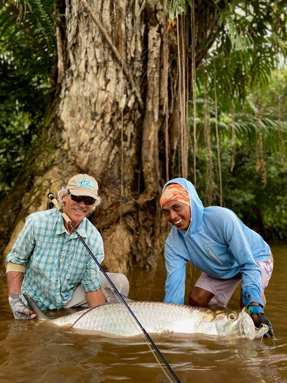 Two men cradle a tarpon in muddy river in Costa Rica 