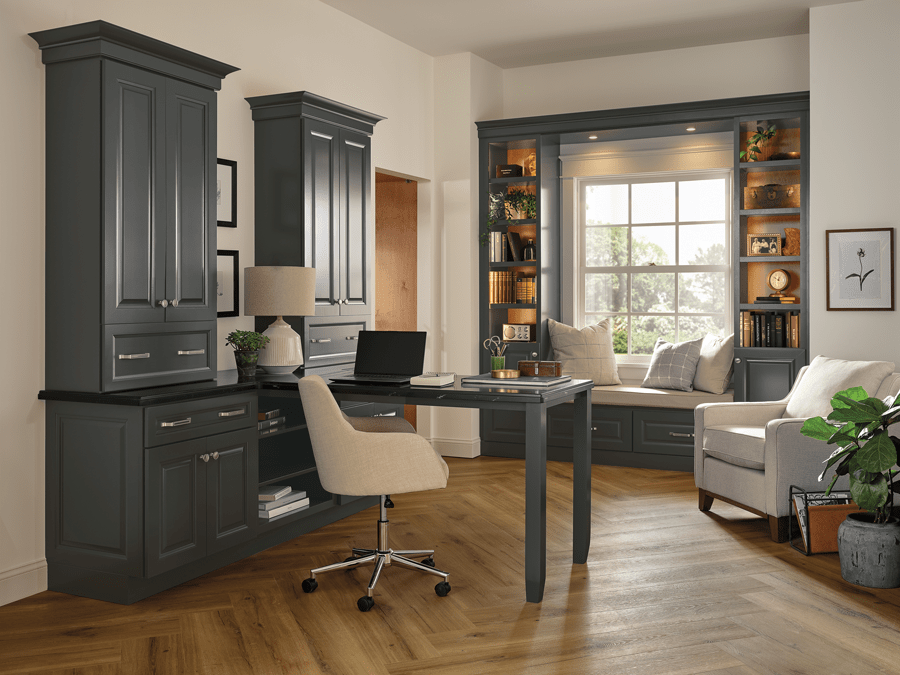 An office space balancing warm wood tones with deep grey cabinetry, showcasing a cozy window-seat and book nook combo