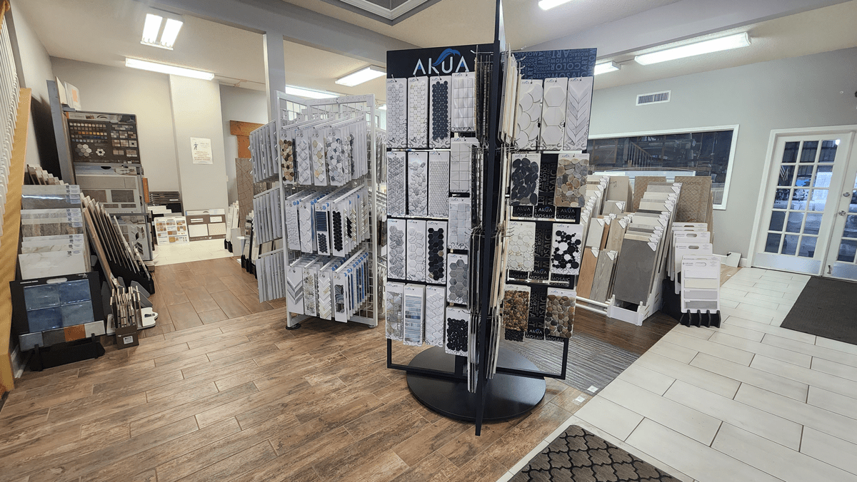 Centered in the image are two displays with cascading samples of decorative mosaics by Akua (right) and Elysium (left), surrounded by other tile products.
