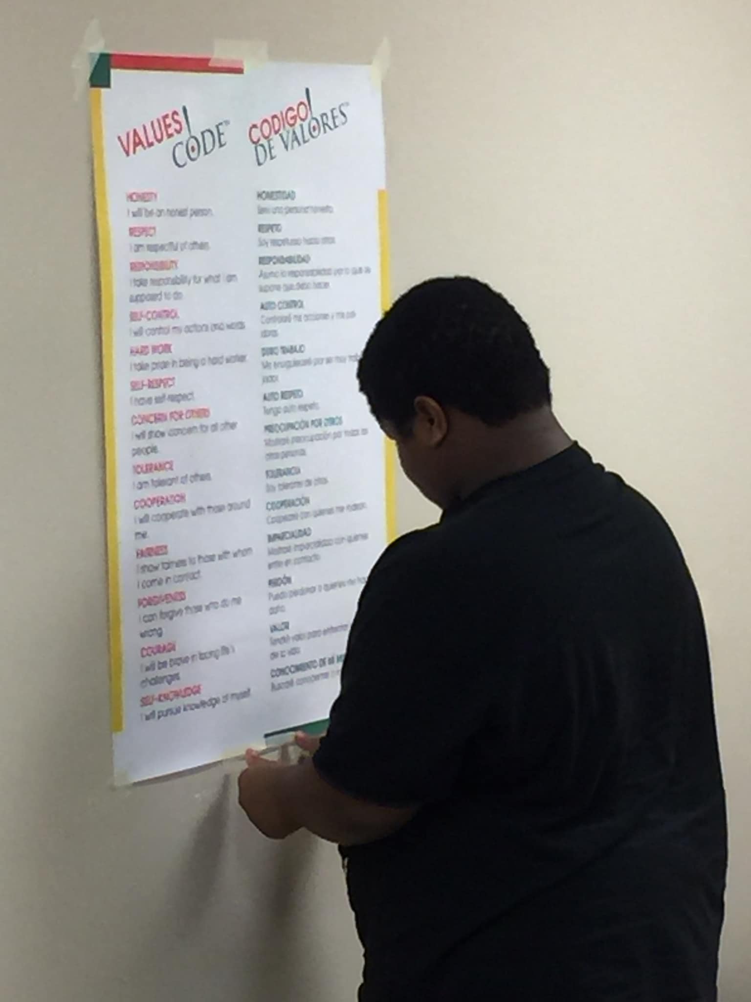 Image of a student from behind putting up a poster of the "Values Code" which issed to teach in classes.