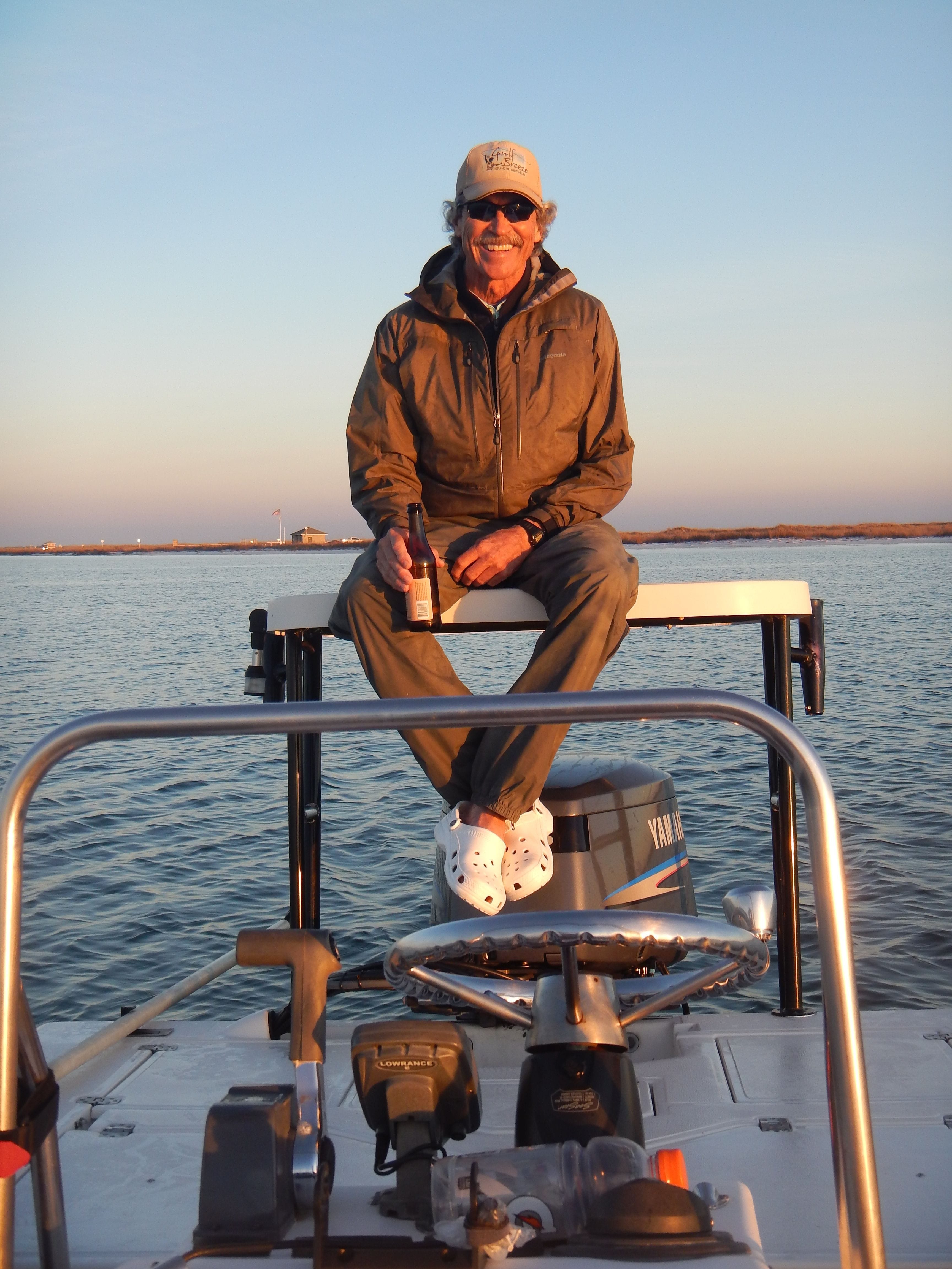 Captain relaxes on the boat at sunset. Entrance to Fort Pickens National Seashore in background.