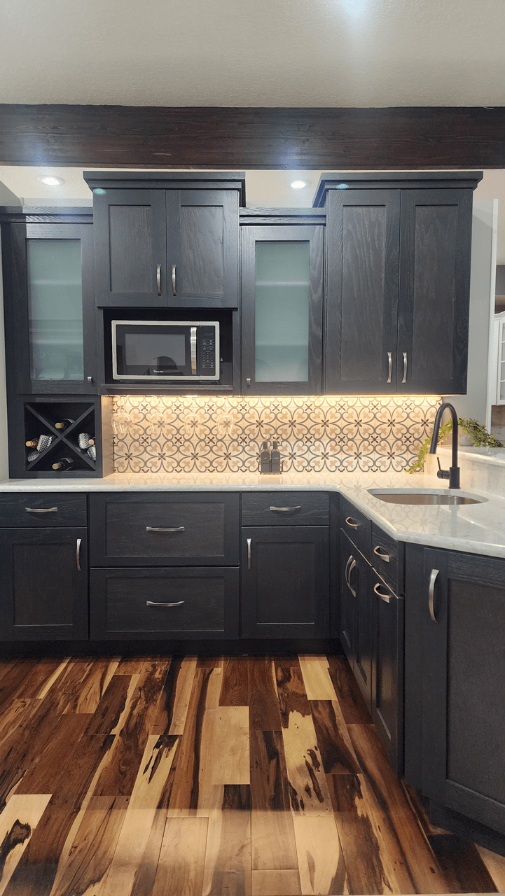 Natural wood grain kitchen cabinetry in a soft black, a mini wine rack, decorative pattern backsplash tile, and frosted glass fronts on two upper cabinet doors.