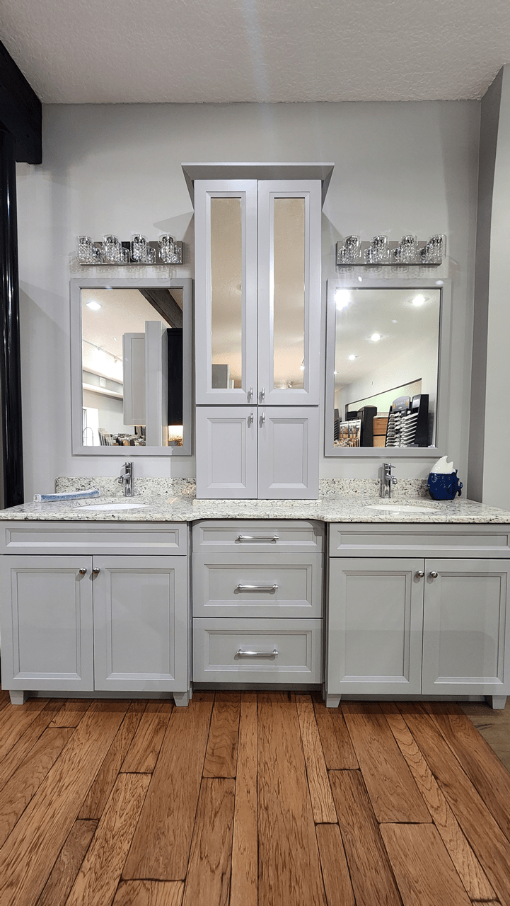 A double bathroom vanity complete with two sinks divided by a cabinet tower with mirrors on the doors and a recessed three drawer base.
