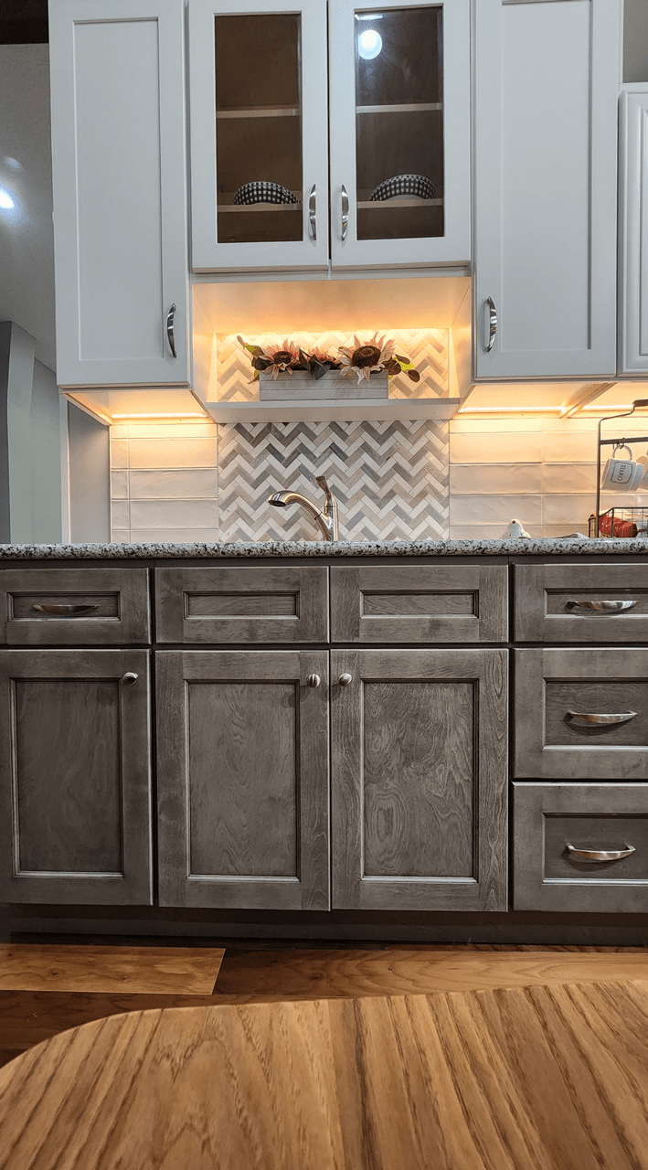 Duotone kitchen in White and Norris Gray split by a stacked elongated white tile featuring a herringbone mosaic tile backsplash behind the sink.