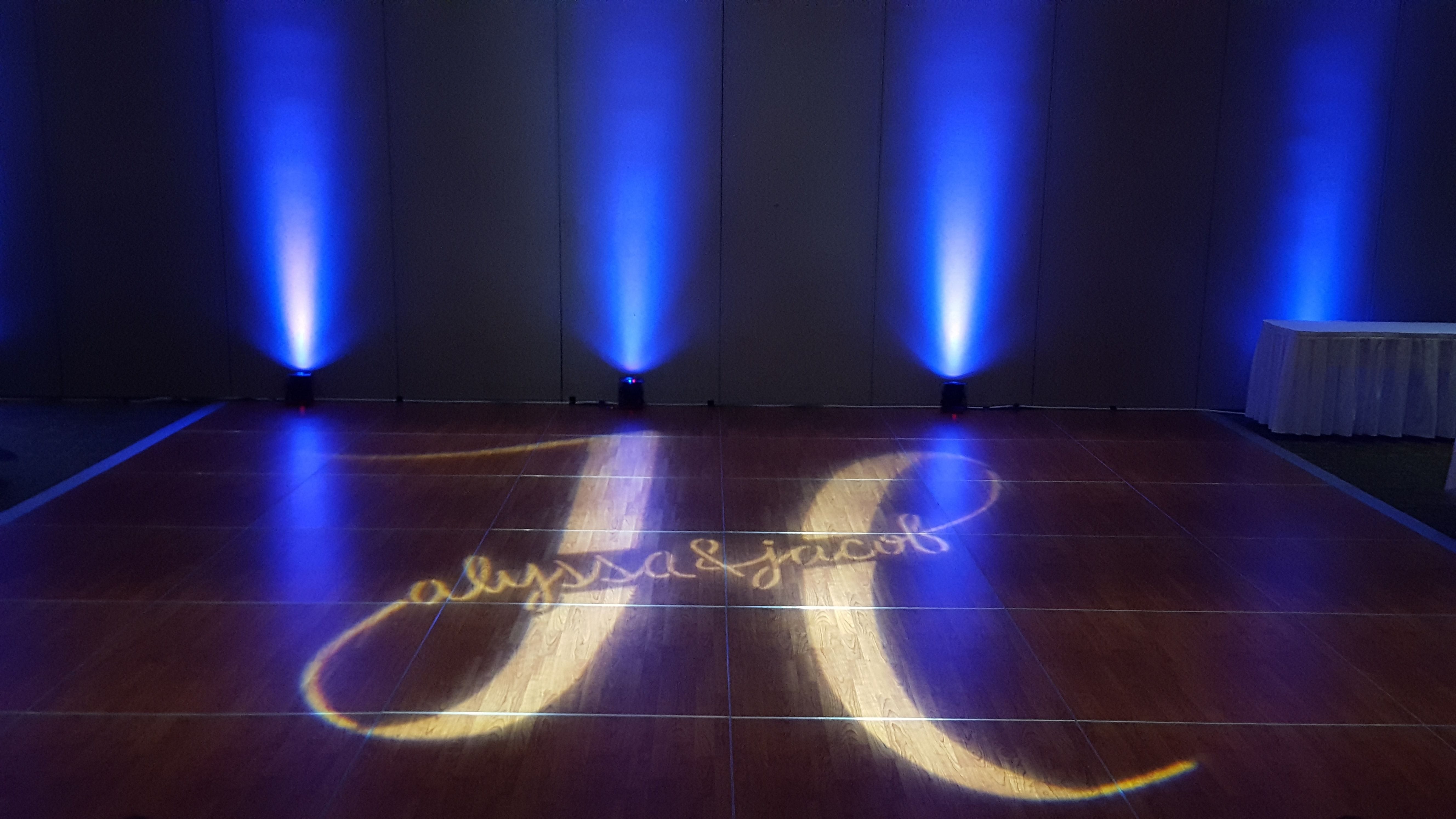 A wedding monogram on the dance floor with purple up lighting in the background.