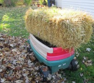 A bale of hay sitting in a child's Little Tike wagon