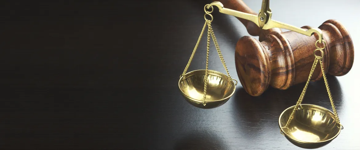 Wooden gavel and a brass balance scale on a dark wood surface