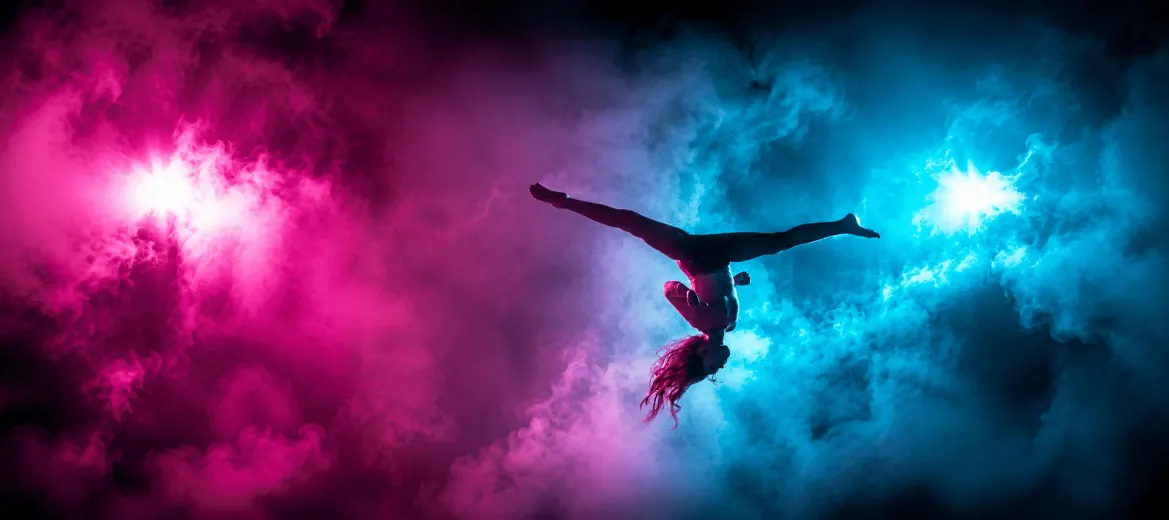 The Extreme Studio Tumbling Athlete Hero Image Athlete performing an inverted aerial skill surrounded by pink and teal smoke at The Extreme Studio, offering tumbling, acro, and cheer classes in Basehor, KS