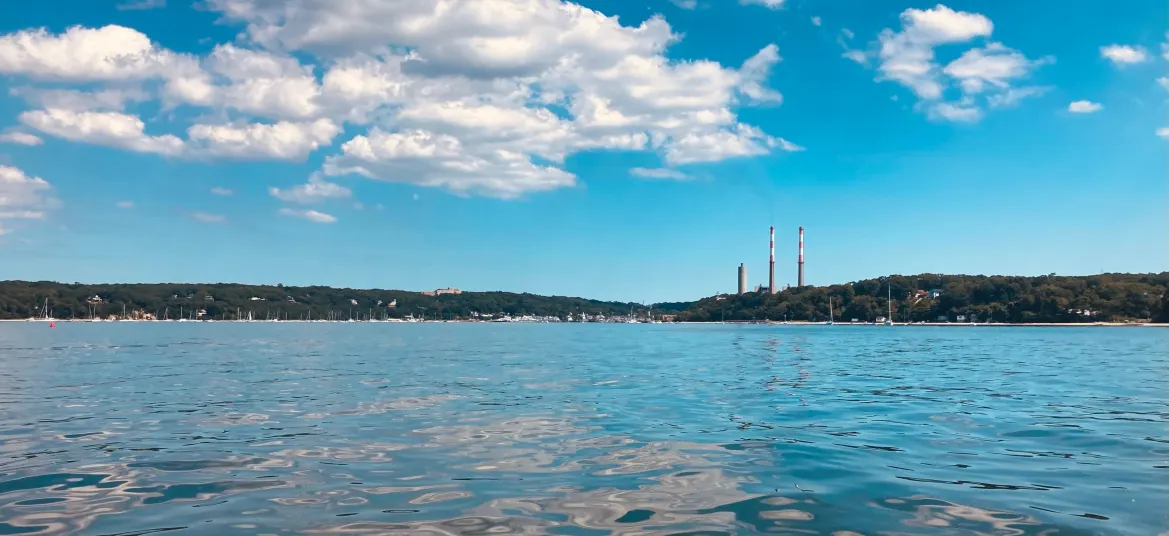 View from water looking inland at Port Jefferson Harbor. Smoke Stacks and St. Charles Hospital are in sight.