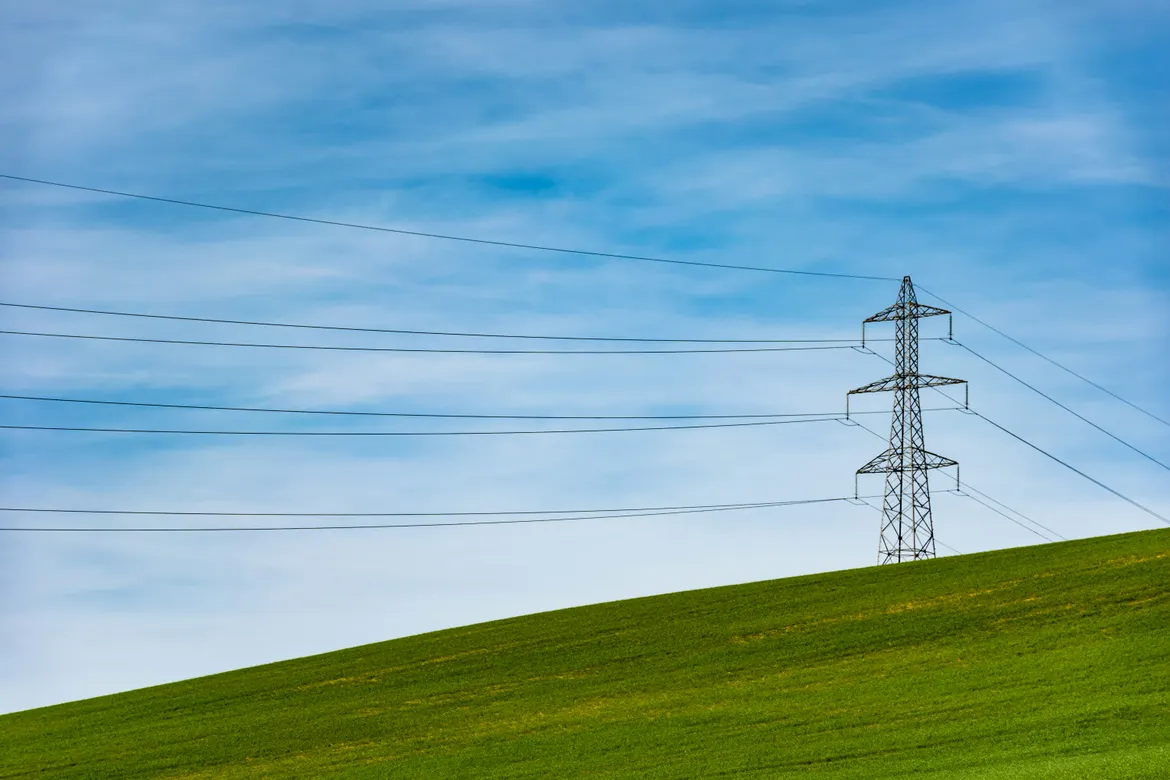 Transmission tower and power lines crossing open green farmland under a blue sky