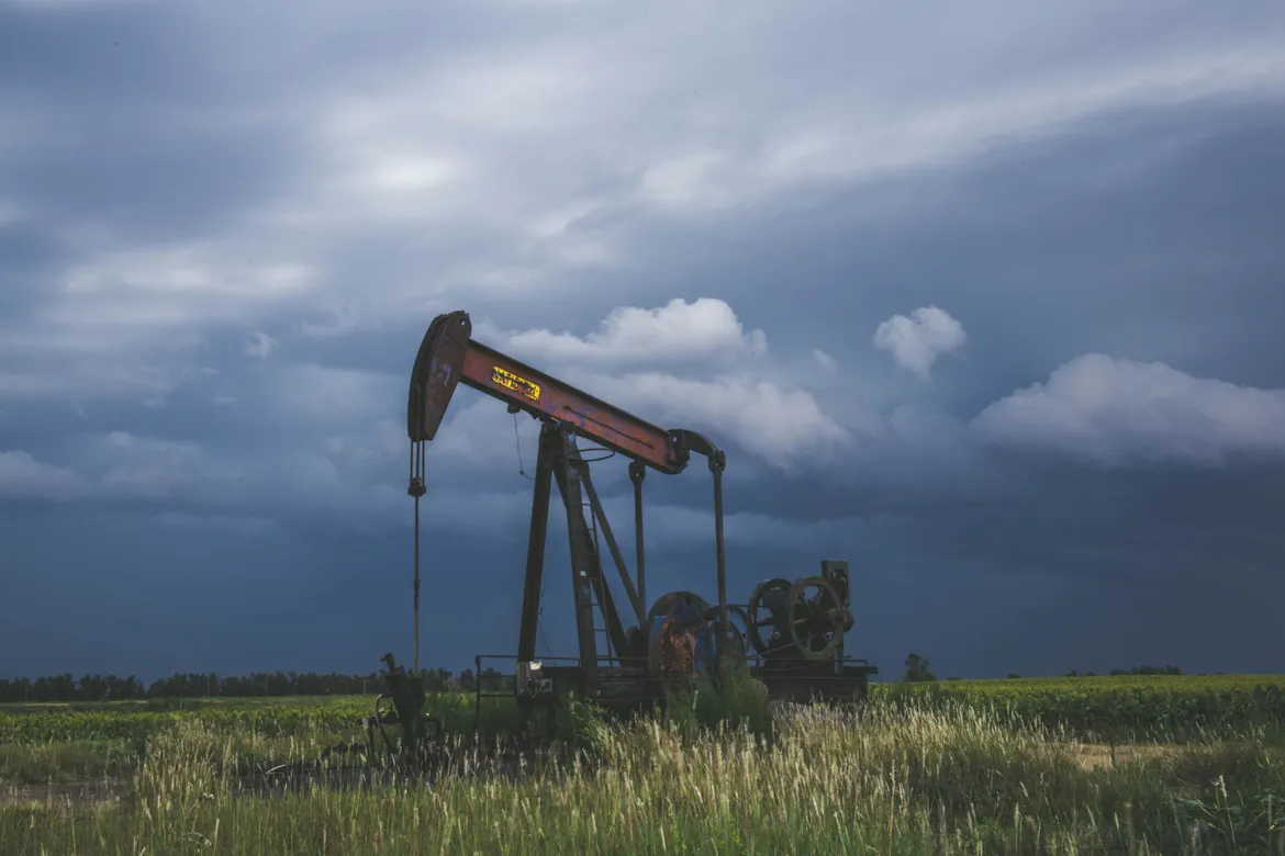 Oil pump jack standing in a grassy field beneath dark storm clouds