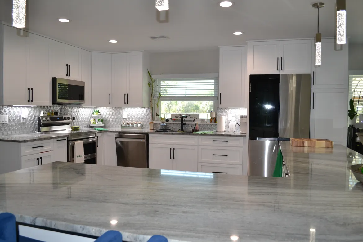 Modern kitchen featuring sleek white cabinets, stainless steel appliances, and a granite countertop. Brightly lit with natural light from a window.