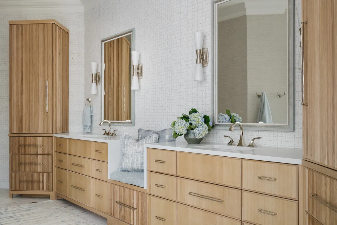 Modern bathroom featuring wooden cabinetry, dual sinks, elegant lighting, and a vase of blue hydrangeas, creating a serene and stylish atmosphere.