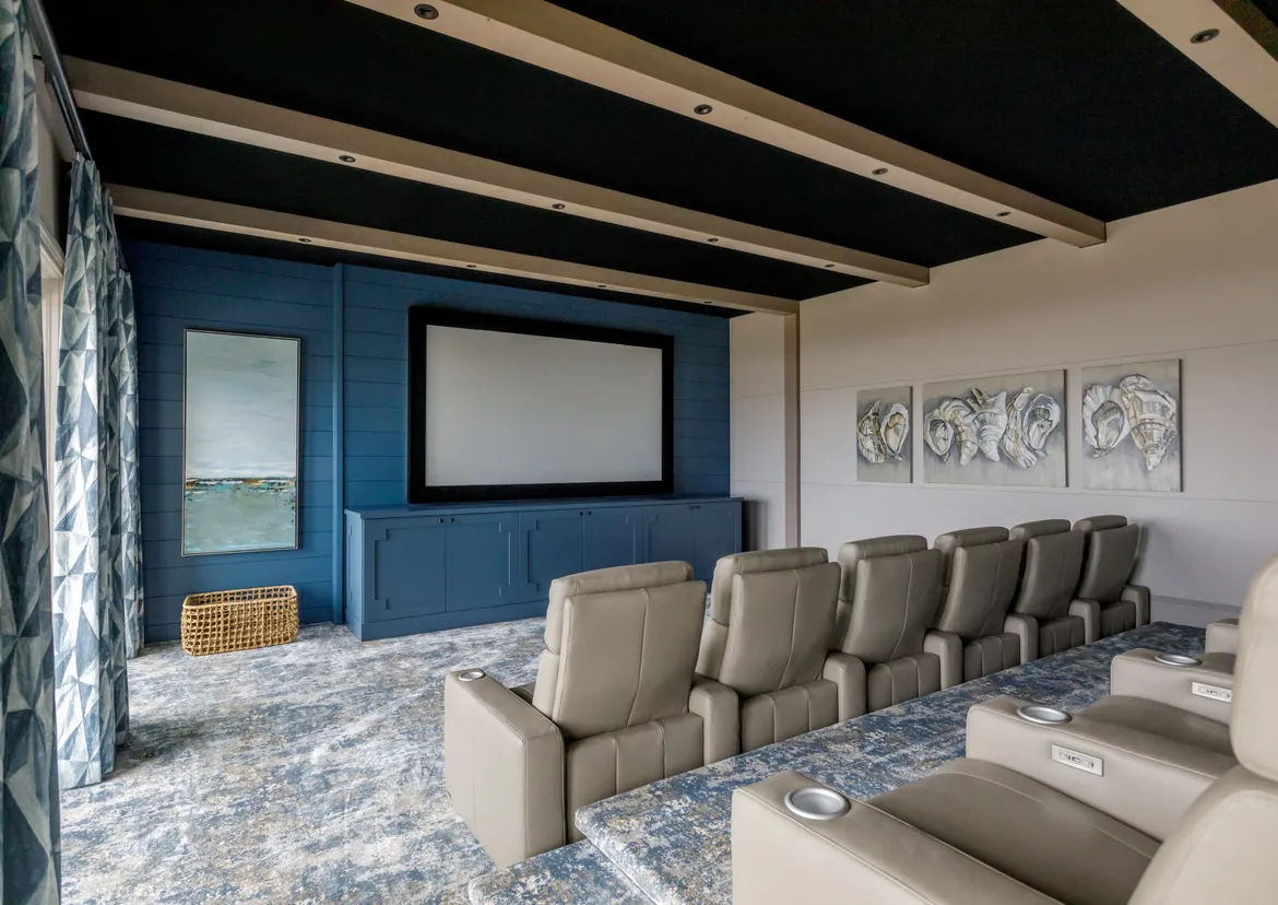 Home theater featuring plush beige seating, a large screen, and nautical-themed wall art, situated in a stylishly designed room.
